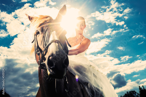 Photo: Bride in wedding dress riding a horse, backlit Bride in wedding dress riding a horse, backlit