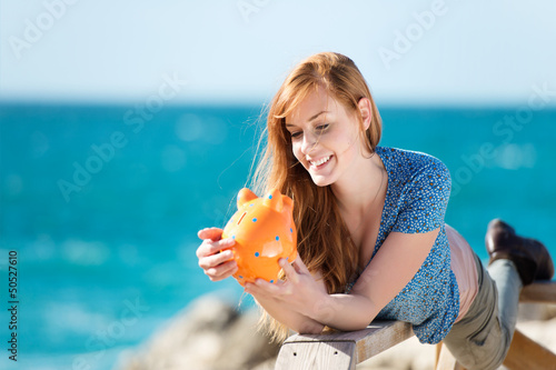 Photo: junge frau mit sparschwein am meer junge frau mit sparschwein am meer