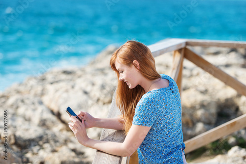 Photo: junge frau am meer schaut auf ihr handy junge frau am meer schaut auf ihr handy