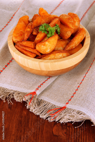 Photo: Appetizing village potatoes in bowl on wooden table close-up Appetizing village potatoes in bowl on wooden table close-up