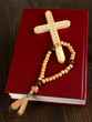 Bible, rosary and cross on wooden table close-up