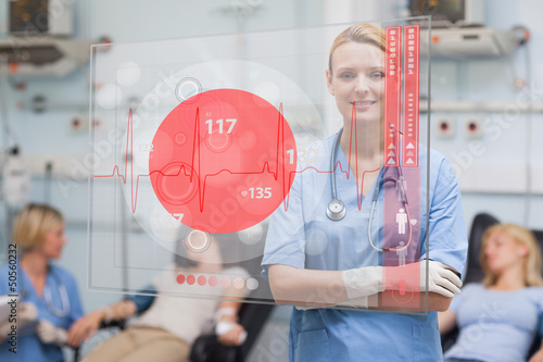 Photo: Smiling nurse standing behind red ECG display screen Smiling nurse standing behind red ECG display screen