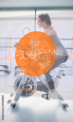 Photo: Woman riding exercise bike with futuristic interface next to her Woman riding exercise bike with futuristic interface next to her