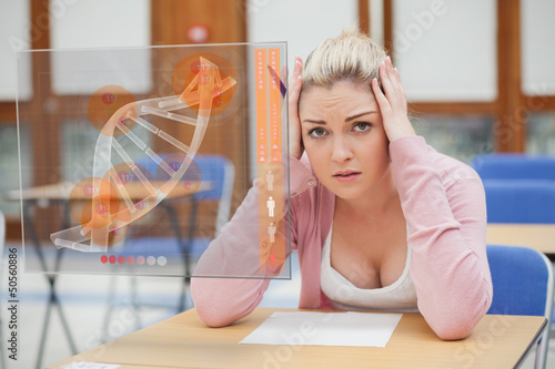 Photo: Blonde woman thinking hard while studying on interface with DNA Blonde woman thinking hard while studying on interface with DNA