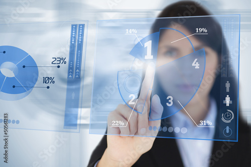 Photo: Serious businesswoman using blue pie chart futuristic interface Serious businesswoman using blue pie chart futuristic interface
