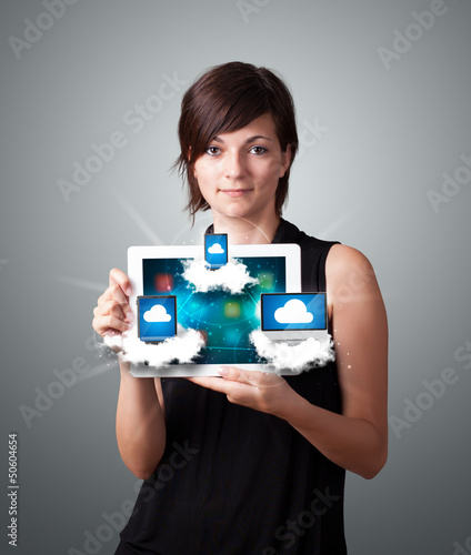 Photo: young woman holding tablet with modern devices in clouds young woman holding tablet with modern devices in clouds