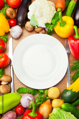 Photo: Organic Vegetables Around White Plate with Knife and Fork Organic Vegetables Around White Plate with Knife and Fork