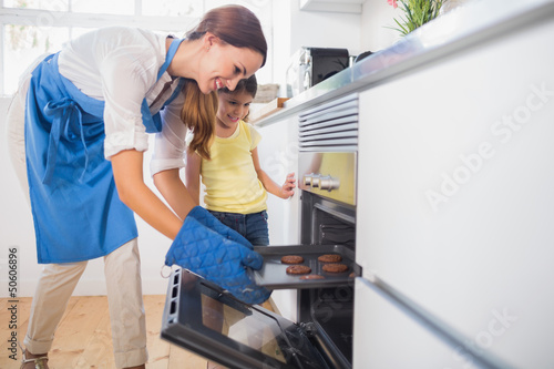 Photo: Smiling mother taking cookies out of the oven Smiling mother taking cookies out of the oven
