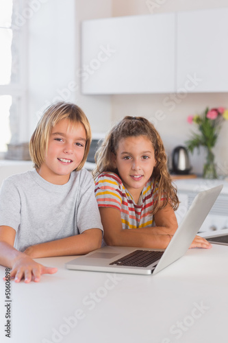 Photo: Two children looking at the camera with laptop in front Two children looking at the camera with laptop in front