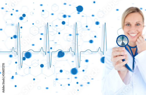 Photo: Blonde doctor holding up stethoscope with blue ECG line Blonde doctor holding up stethoscope with blue ECG line