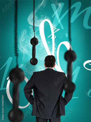 Photo: Businessman looking at hanging black telephone receiver Businessman looking at hanging black telephone receiver