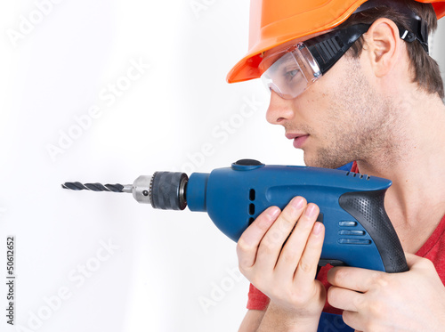 Photo: A man drilling a hole in the wall. A man drilling a hole in the wall.