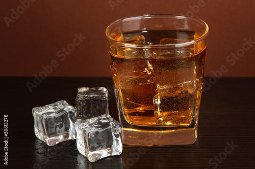 Photo: Glass of whiskey and ice on brown background Glass of whiskey and ice on brown background