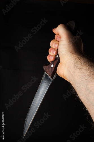Photo: Hairy male hand holding a knife over a black background Hairy male hand holding a knife over a black background