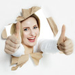 Pretty woman with thumbs up smiling through paper hole