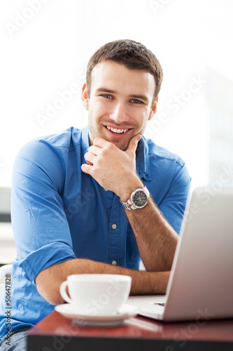 Photo: Young man using laptop in cafe Young man using laptop in cafe