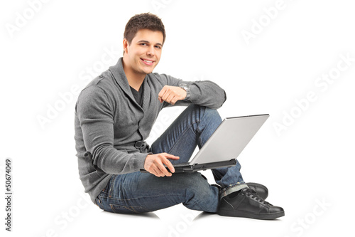 Photo: Handsome guy working on a laptop and sitting on a floor Handsome guy working on a laptop and sitting on a floor