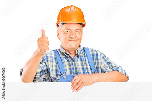 Photo: Mature worker with helmet posing behind a panel with thumb up Mature worker with helmet posing behind a panel with thumb up