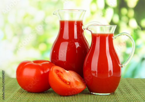 Photo: Tomato juice in pitchers on table on bright background Tomato juice in pitchers on table on bright background