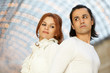 Dark-haired man and red-haired woman stand back to back and look