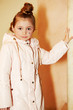 Girl in light coat stands, leaning one hand on marble pillar