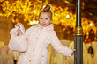 Girl in light coat stands, leaning one hand