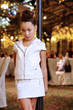 Girl in white leather suit stands near decorative lamppost