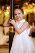 Little girl in white evening dress stands smiling slightly