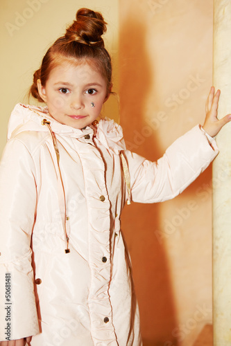 Photo: Girl in light coat stands, leaning one hand on marble pillar Girl in light coat stands, leaning one hand on marble pillar