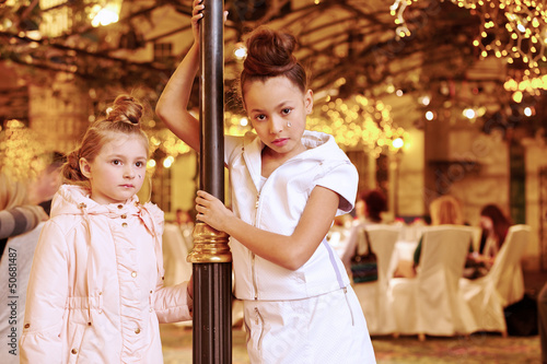 Photo: Girls stand near decorative lamp post, one in light coat Girls stand near decorative lamp post, one in light coat
