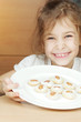 Smiling little girl holds plate with cookies with almonds