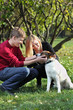 Photo: Happy couple smile and touch dog in park at sunny autumn day. Happy couple smile and touch dog in park at sunny autumn day.