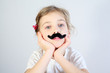 Little melancholy girl in white with glued fake black mustache.