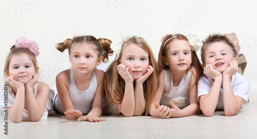 Photo: Five cute little children in white clothes lie on floor and look Five cute little children in white clothes lie on floor and look