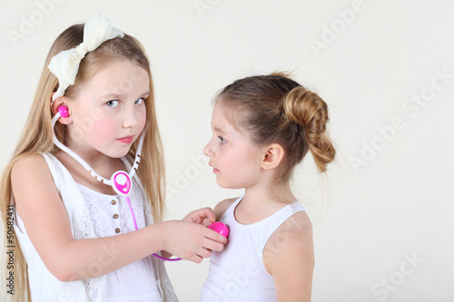 Photo: Little girl in white dress listens heartbeat of another girl Little girl in white dress listens heartbeat of another girl