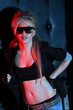 Young woman rocker in big sunglasses with tattoo poses near wall