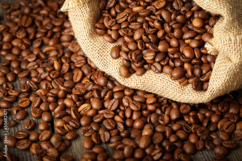 Photo: Coffee beans in coffee bag made from burlap on wooden surface. Coffee beans in coffee bag made from burlap on wooden surface.