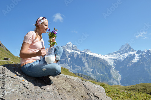 Photo: Girl holding a jug of milk and flowers against Swiss Alps Girl holding a jug of milk and flowers against Swiss Alps