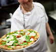 The chief the cook holding the whole pizza in a hand