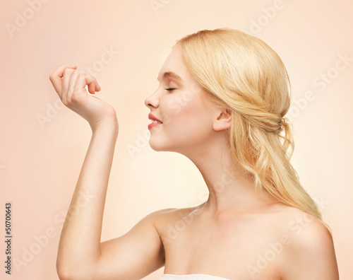 Photo: young girl smelling pefrume on her hand young girl smelling pefrume on her hand