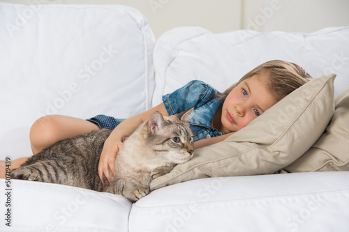Photo: Little girl laying on sofa with her tabby cat Little girl laying on sofa with her tabby cat