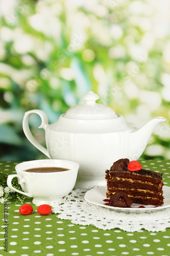 Photo: Teapot, cup of tea and delicious cake on natural background Teapot, cup of tea and delicious cake on natural background