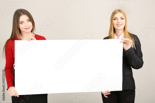 Photo: Two business women with blank form on grey background Two business women with blank form on grey background