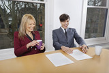 Photo: Cheerful young businesspeople with coffee mugs and documents at conference table Cheerful young businesspeople with coffee mugs and documents at conference table