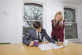 Photo: Young businesswoman looking at male colleague signing documents at conference table Young businesswoman looking at male colleague signing documents at conference table