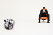Photo: Worried businessman on chair and piggybank tied with rope representing financial difficulties Worried businessman on chair and piggybank tied with rope representing financial difficulties