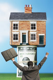 Photo: Back view of victorious businessman with briefcase in front of house on money rolls Back view of victorious businessman with briefcase in front of house on money rolls