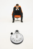 Photo : Worried businessman sitting on chair with stopwatch representing loss of time Worried businessman sitting on chair with stopwatch representing loss of time