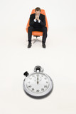 Photo : Anxious businessman sitting on chair with stopwatch in front of him representing loss of time Anxious businessman sitting on chair with stopwatch in front of him representing loss of time