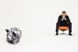 Photo: Pensive businessman on chair and piggybank tied with rope representing financial difficulties Pensive businessman on chair and piggybank tied with rope representing financial difficulties